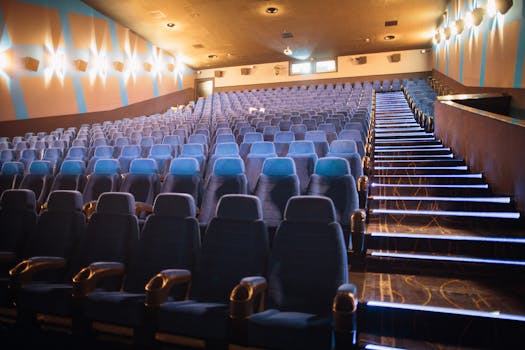 A spacious cinema hall with empty rows of blue seats and illuminated stairs, indoors.