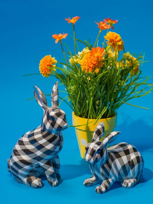 Free Vibrant spring-themed decor featuring plaid rabbit figurines and bright orange flowers against a blue background. Stock Photo