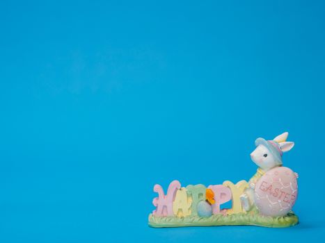 Cute Easter bunny figurine with 'Happy Easter' text on a blue backdrop, ideal for holiday design.