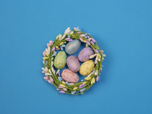 Free Colorful Easter eggs in a pastel wreath on a bright blue background. Perfect for festive decor. Stock Photo
