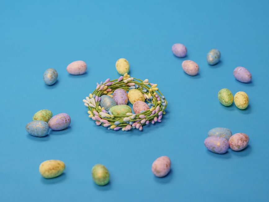 Festive arrangement of pastel Easter eggs and wreath on a vibrant blue backdrop.