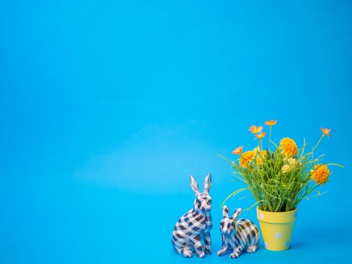 Free Colorful spring setup featuring ceramic bunnies and flowers against a blue background. Stock Photo