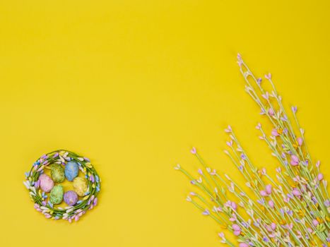 Festive Easter nest with painted eggs and flowers on bright yellow background.