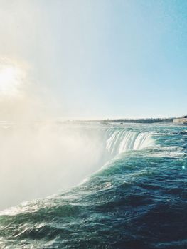 Capture the majestic Niagara Falls with mist rising under a clear blue sky.
