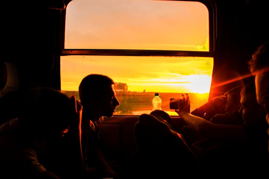 Silhouette of people on a train capturing a vivid sunset through a window.