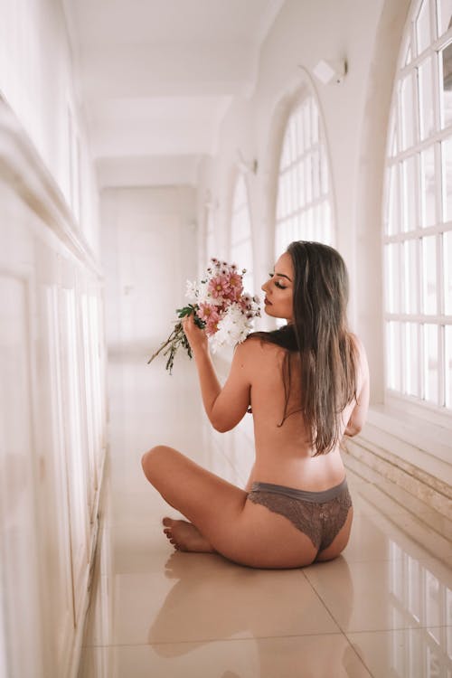 Free Back view full body of sexy gentle female wearing underpants and smelling aromatic fresh chrysanthemums sitting on floor in hallway Stock Photo