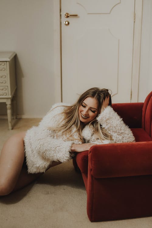 High angle of positive of female wearing soft clothes sitting near armchair and laughing happily and leaning on hand