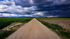 一条土路穿过郁郁葱葱的绿色田野，在阴沉的天空下延伸