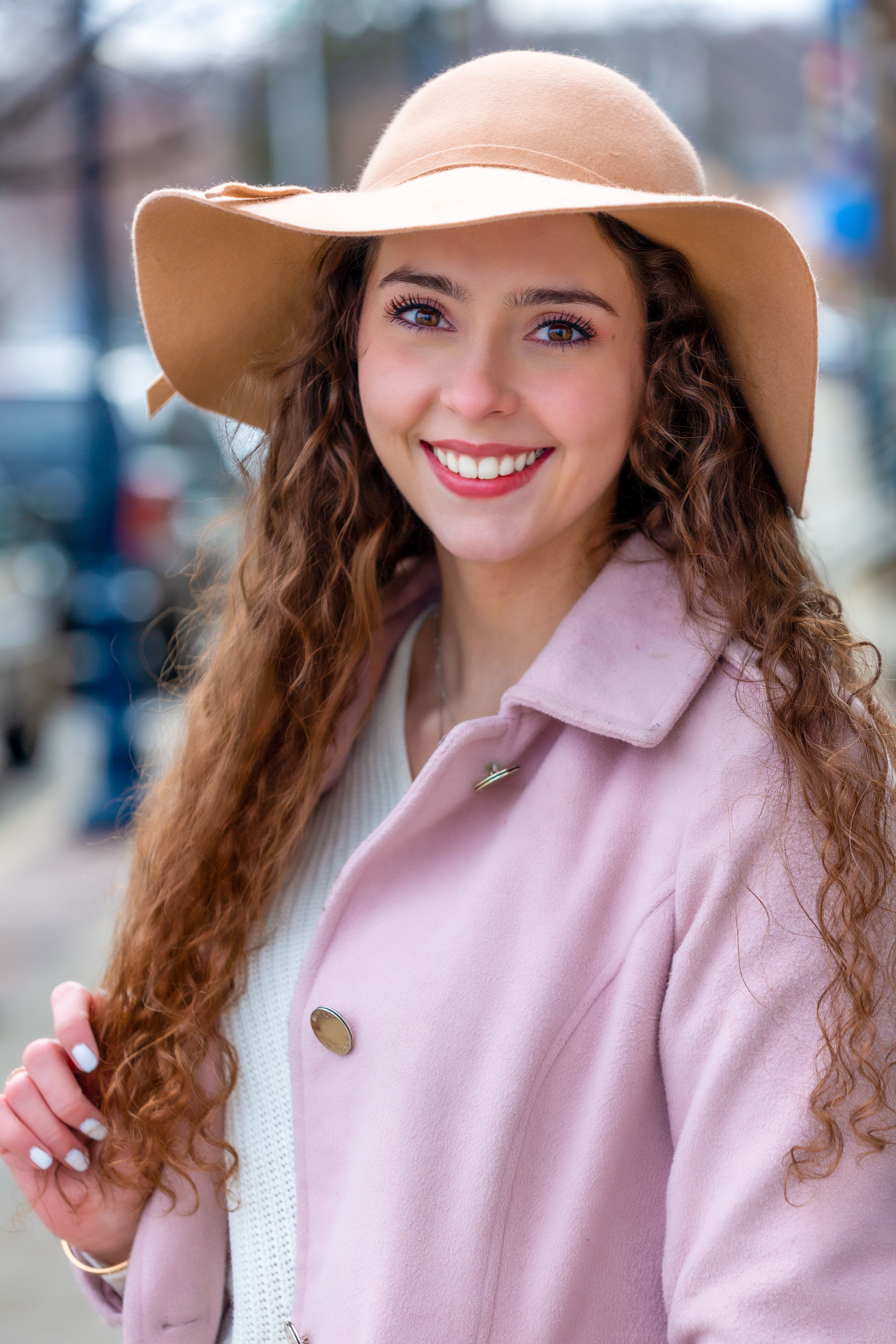 Charming portrait of a woman in a pink coat and hat, smiling warmly.