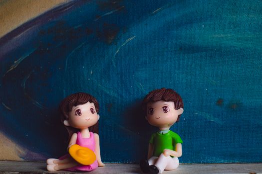 Small plastic figures of man with girlfriend sitting against canvas with artwork of blue ocean
