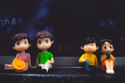 Small plastic statuettes of women near boyfriends in bright apparel with hat and book sitting on portable computer