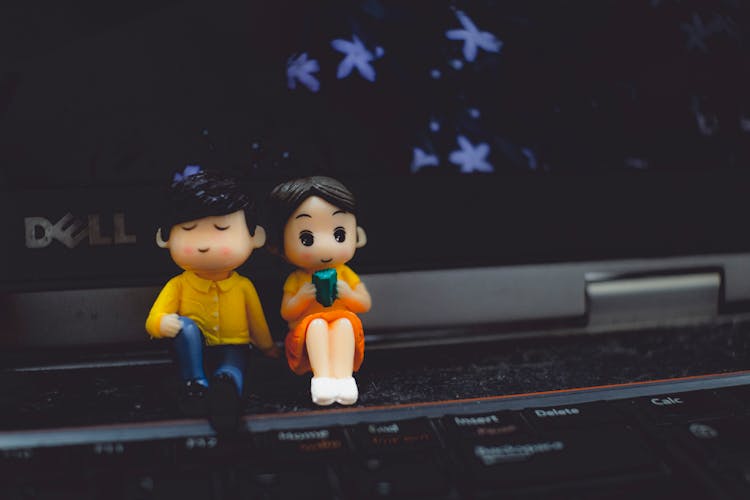 Statuettes Of Couple With Book Against Laptop Screen