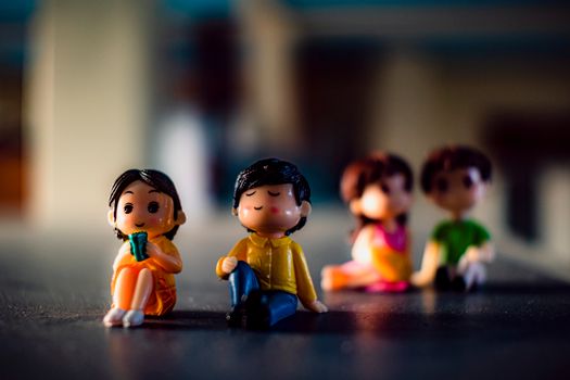 Small plastic figures of men with girlfriends in bright clothes sitting in shiny light on blurred background