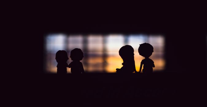 Silhouettes of cute small figurines with boys and girls placed together in dark room against big window in evening time