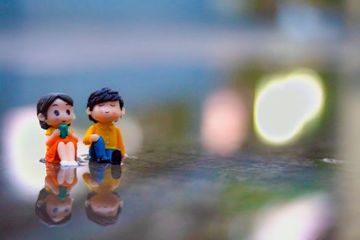 Small decorative figurines of boy and girl placed on walkway on street with bright lights in city against blurred background