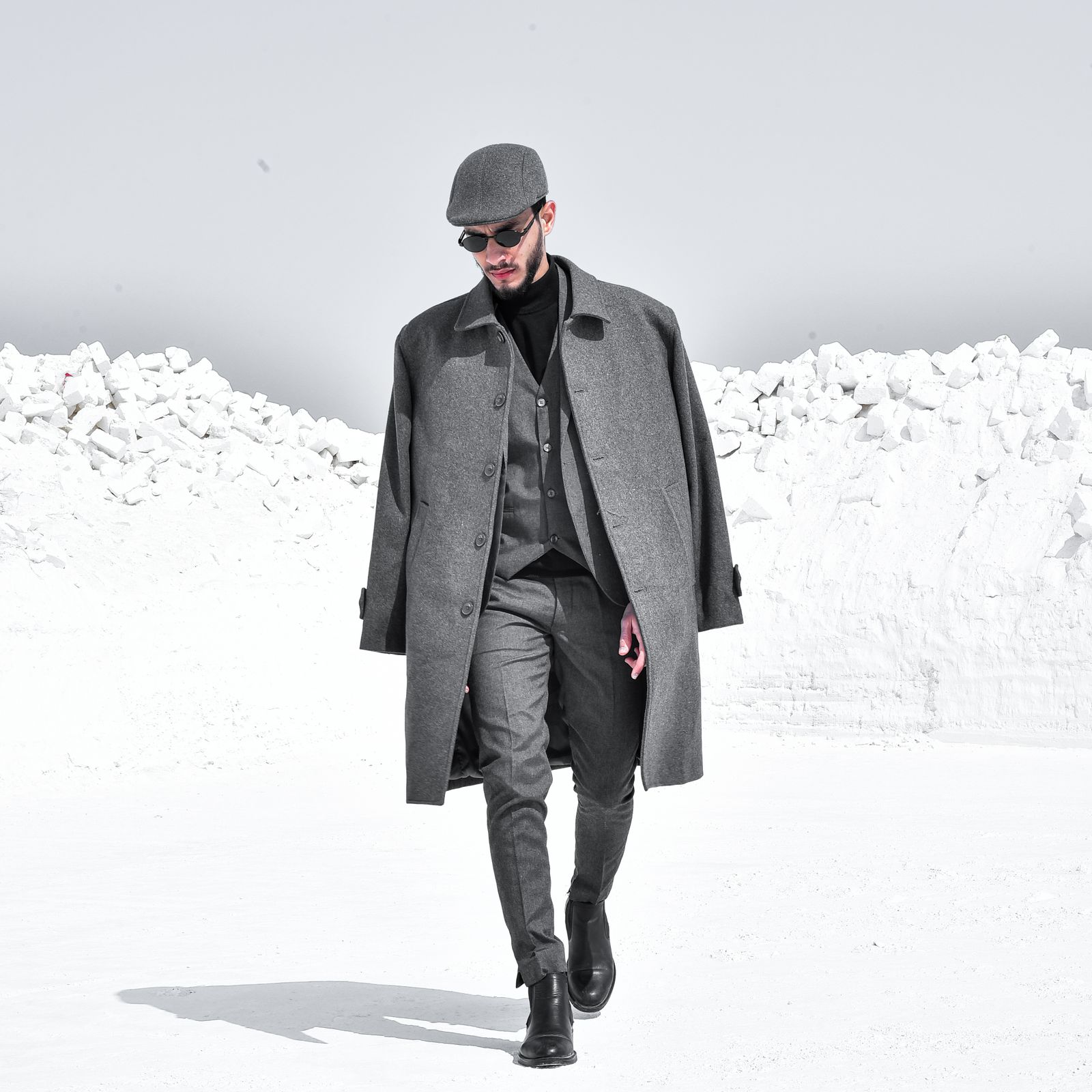 Model in a heavy grey coat walking through a frosty winter landscape