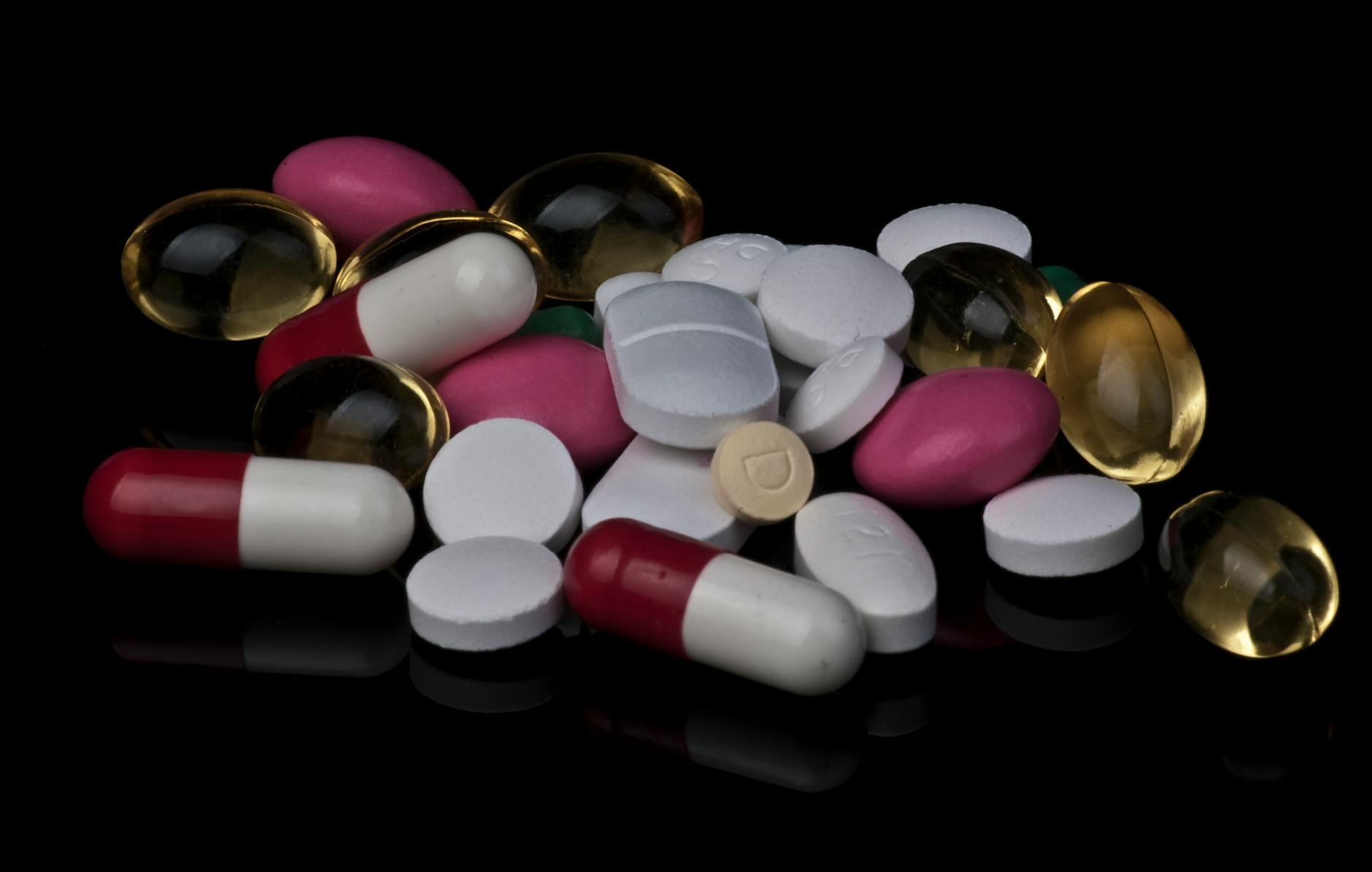 Close-up of various colorful pills and capsules on a black background.