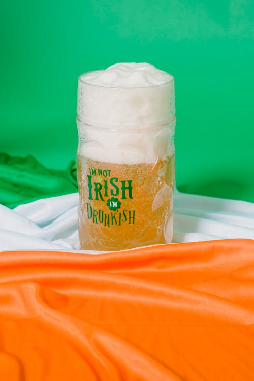 Glass of traditional Irish beer with froth placed on flag of Ireland on green background