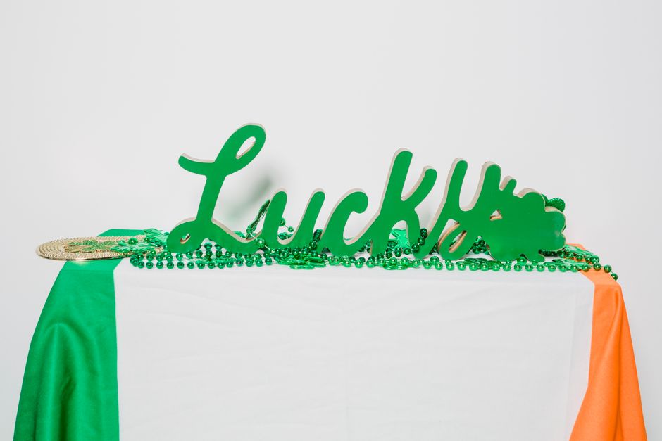 Green 'Lucky' sign adorned with beads on a table with an Irish flag, celebrating St. Patrick's Day.