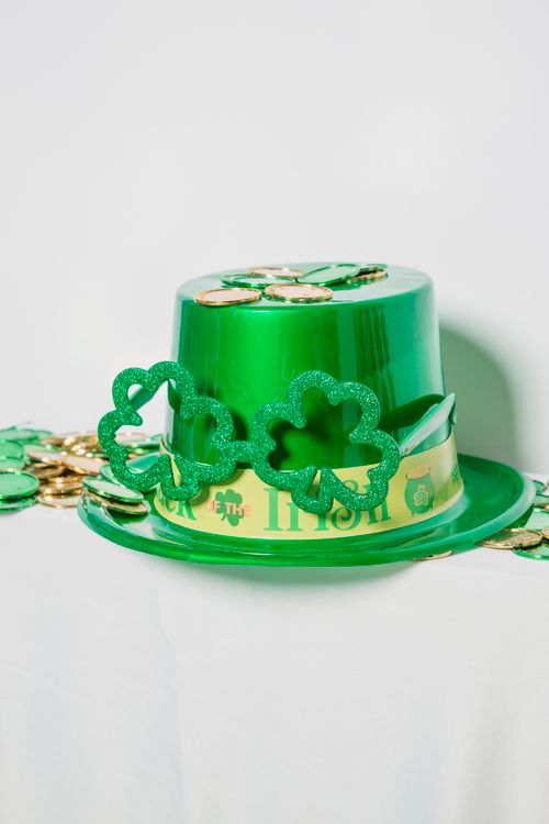 Free Shiny green hat with decorations and clover placed near heap of colorful coins on white background Stock Photo