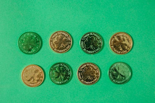 Top view of gold coins with clover pattern arranged in rows on light green surface