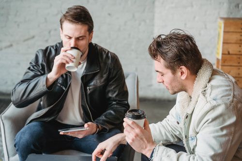 Free Modern adult men in warm jackets sitting together in armchairs at table and drinking coffee in cafe Stock Photo