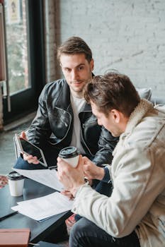 Two men discussing business papers over coffee in a trendy café.