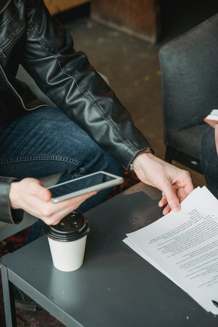 Man With Smartphone Reading Document While Sitting At Table