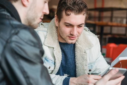 Free Male worker looking at screen of tablet while discussing strategy of project with crop partner in cafe Stock Photo