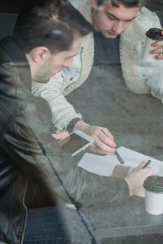 Through glass high angle of crop concentrated young male colleagues pointing at document during business meeting
