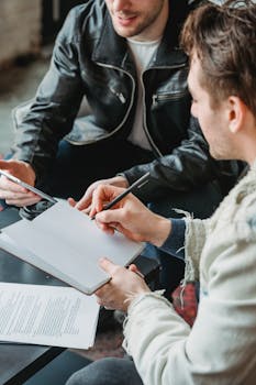 Two men engage in a collaborative business meeting, taking notes and discussing strategies.