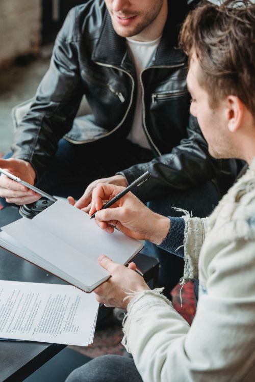Free From above of crop entrepreneur taking notes in planner while discussing startup with partner browsing tablet Stock Photo