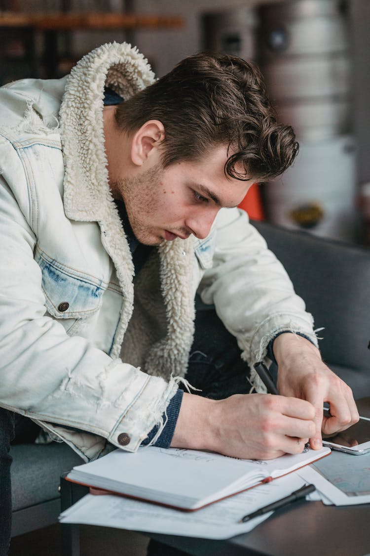 Concentrated Man Writing Notes In Notebook While Working Remotely