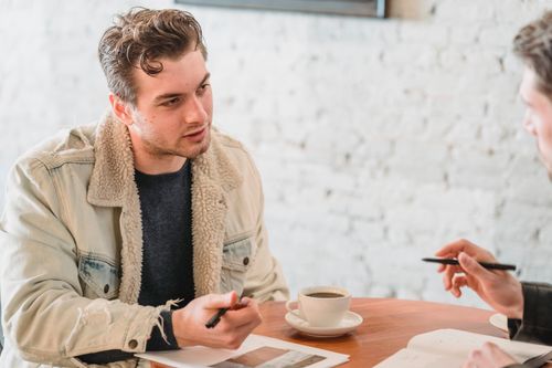 Free Concentrated businessmen sitting at table with cups of coffee and documents while discussing details of project Stock Photo