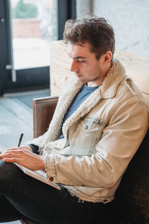 Free Serious male in stylish beige warm jacket writing in notebook on blurred background in daylight Stock Photo