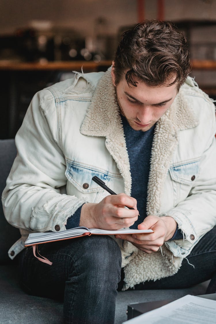 Trendy Writer Writing In Notebook On Sofa