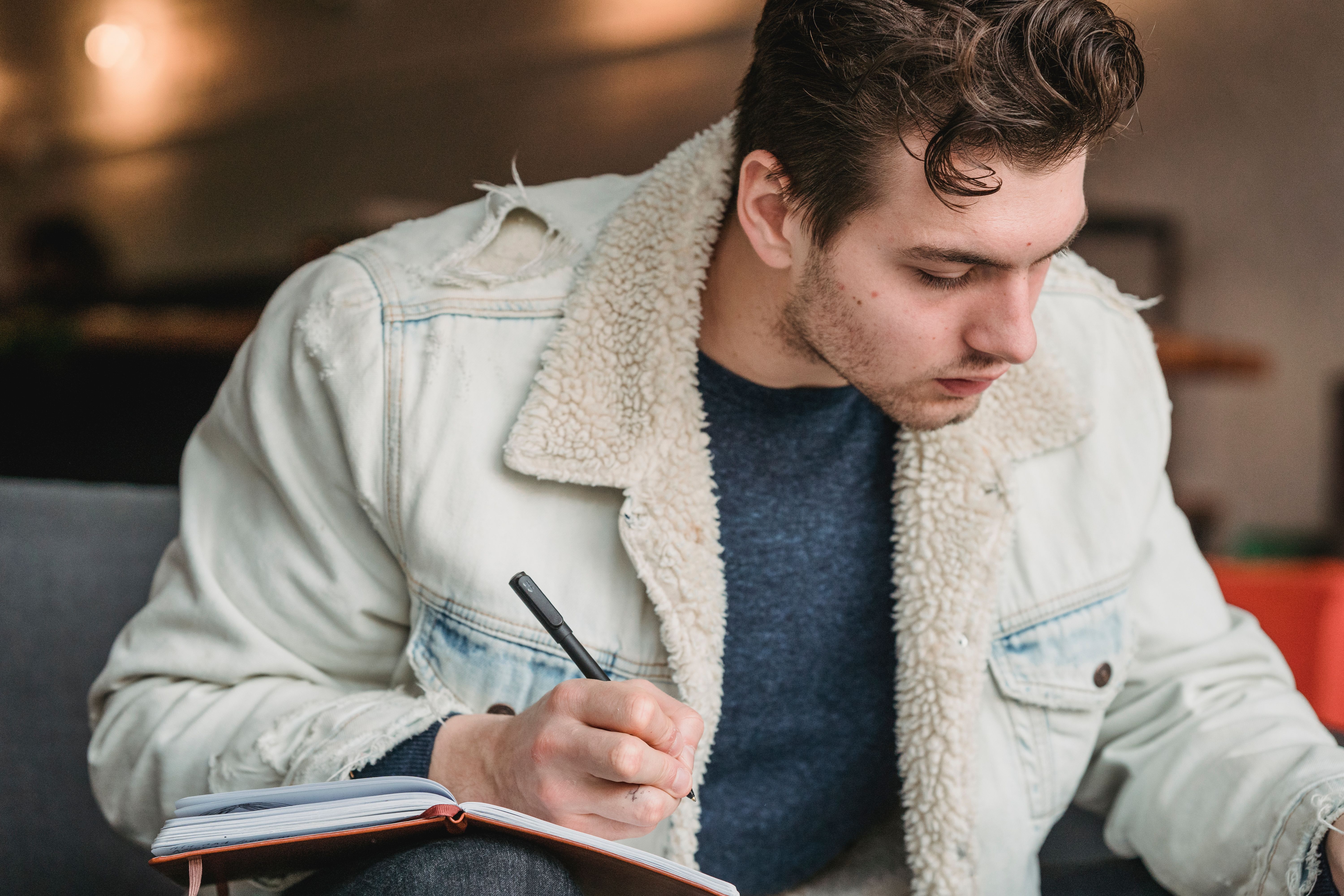 Crop serious male with fashionable hairstyle taking notes in planner on blurred background of cafeteria