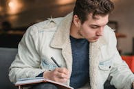 Thoughtful man in trendy jacket writing in planner