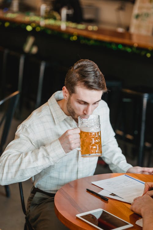 Pensive businessman drinking beer at table with papers near partner