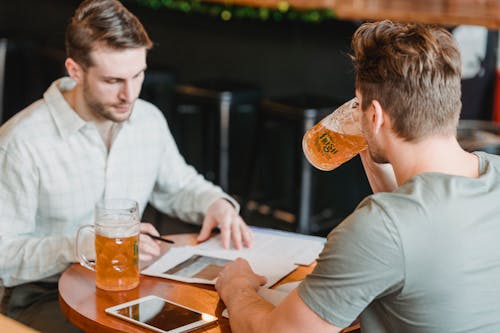 Free Focused colleagues drinking glasses with beer at table with papers and tablet with black screen on blurred background Stock Photo