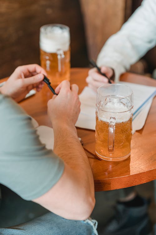 Crop unrecognizable men with pens and important papers at table on blurred background in pub