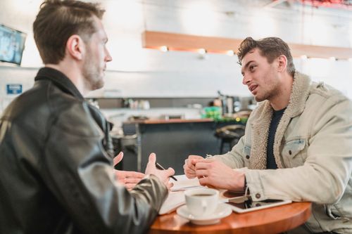 Free Side view of crop young man talking about business project at table with papers and looking at partner on blurred background Stock Photo
