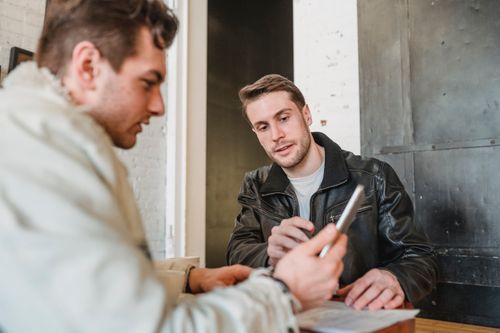 Free Crop colleague working with tablet while coworker in black leather jacket telling about new project Stock Photo