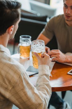 Crop colleagues drinking beer from glasses at table with important papers on blurred background