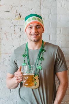Cheerful young man with beer and festive attire celebrating St. Patrick's Day indoors.