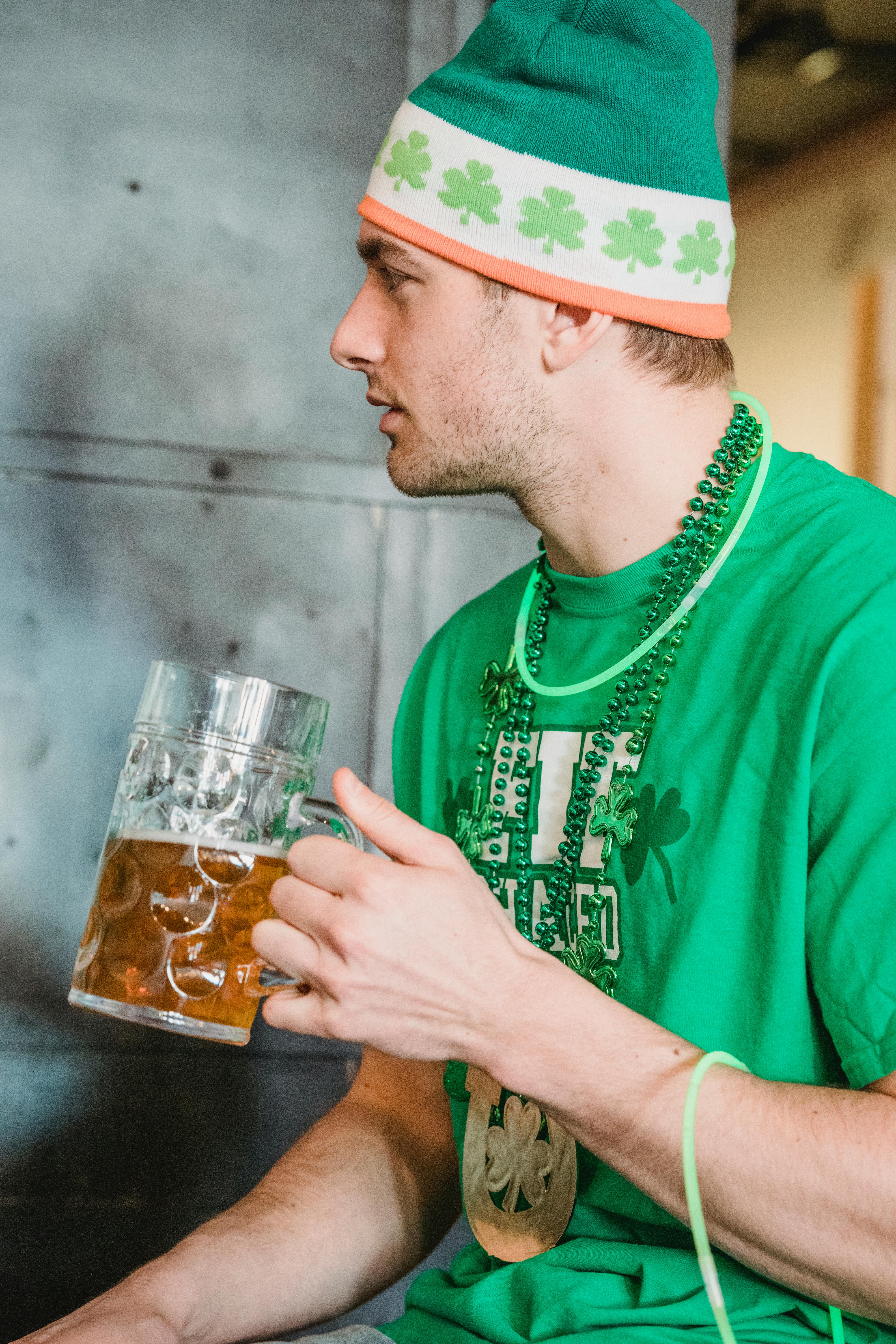 Man in festive green attire enjoying a beer on St. Patrick's Day indoors.