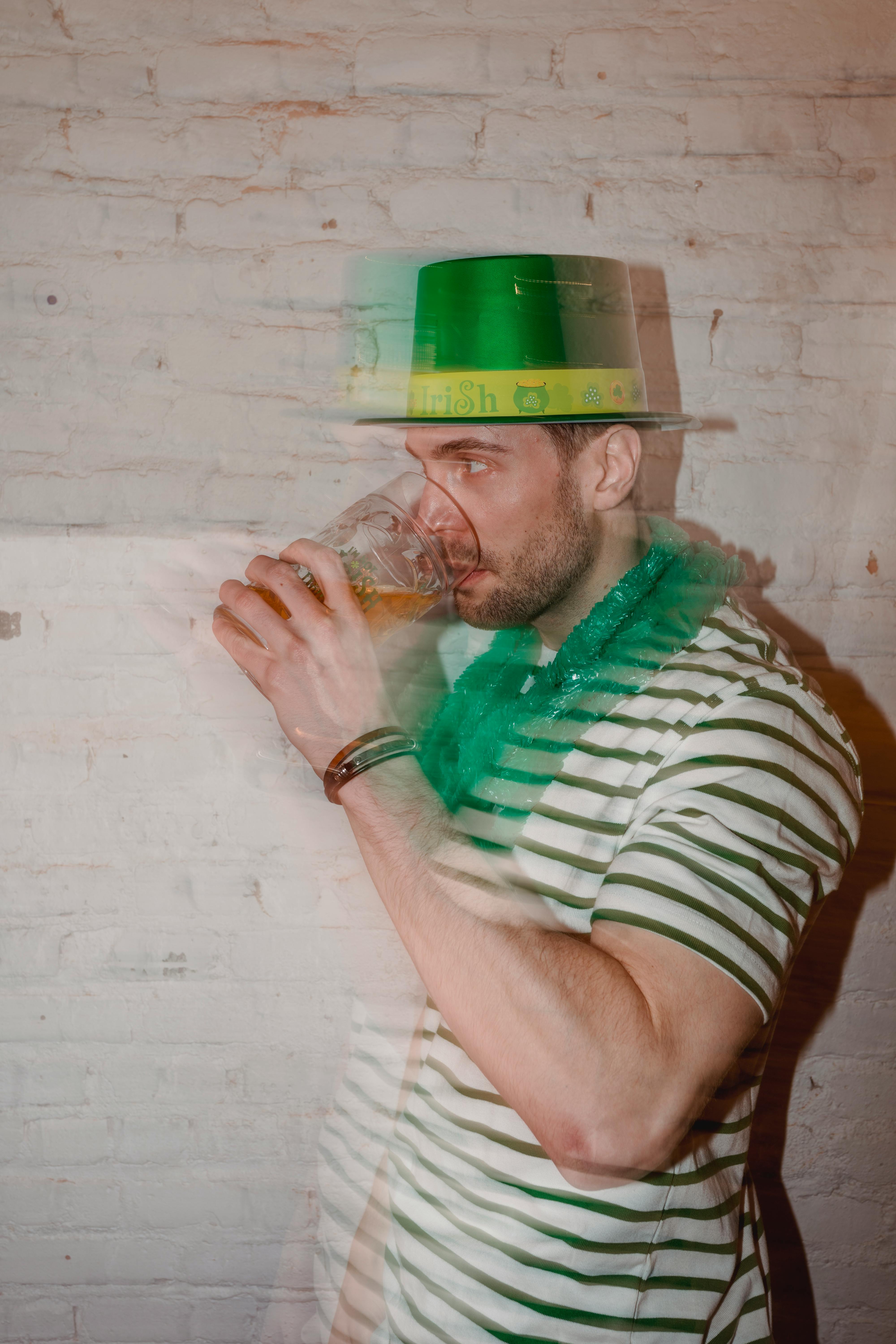 Through glass wall view of male in shamrock hat enjoying beer while looking away on St Paddys Day
