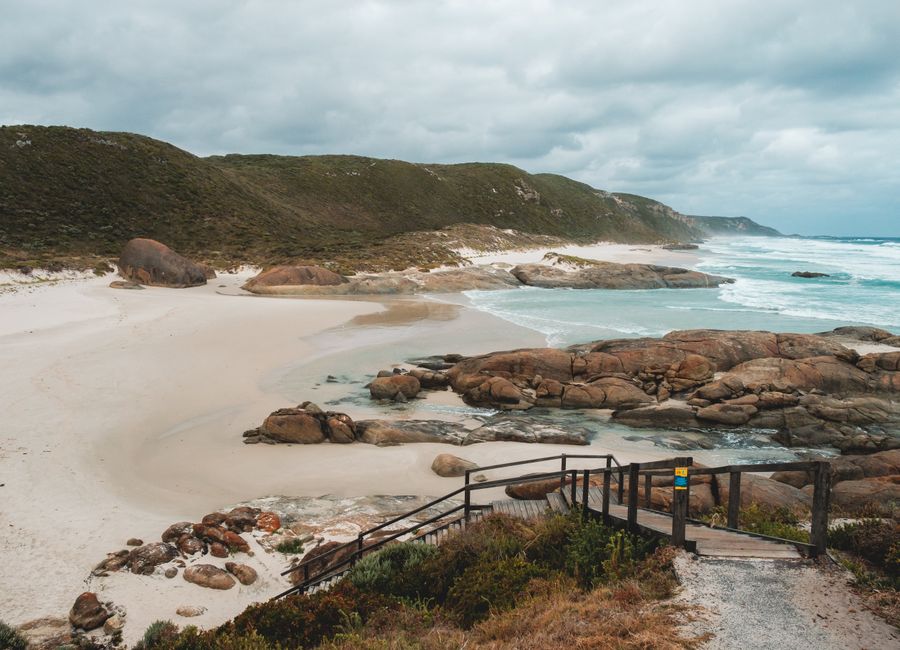 Amazing scenery on wide sandy Lights Beach with rocky formations and grassy hill washing by foamy ocean against cloudy sky in Albany