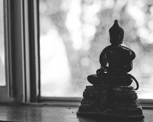 Black and white small statuette of Buddha sitting in Lotus Pose placed on windowsill