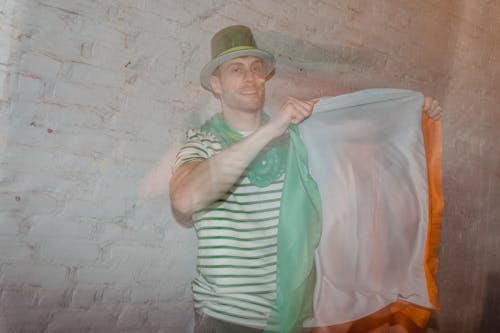 Adult male in shamrock hat with national flag of Ireland looking at camera on St Paddys Day behind glass wall